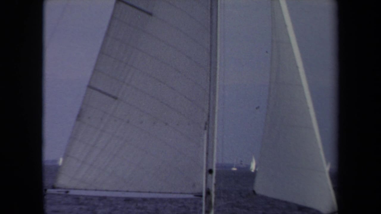 From aboard a sailboat in 1970 Annapolis, large sails and rigging frame distant boats under a muted sky.
