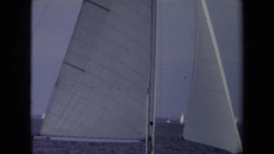 From aboard a sailboat in 1970 Annapolis, large sails and rigging frame distant boats under a muted sky.