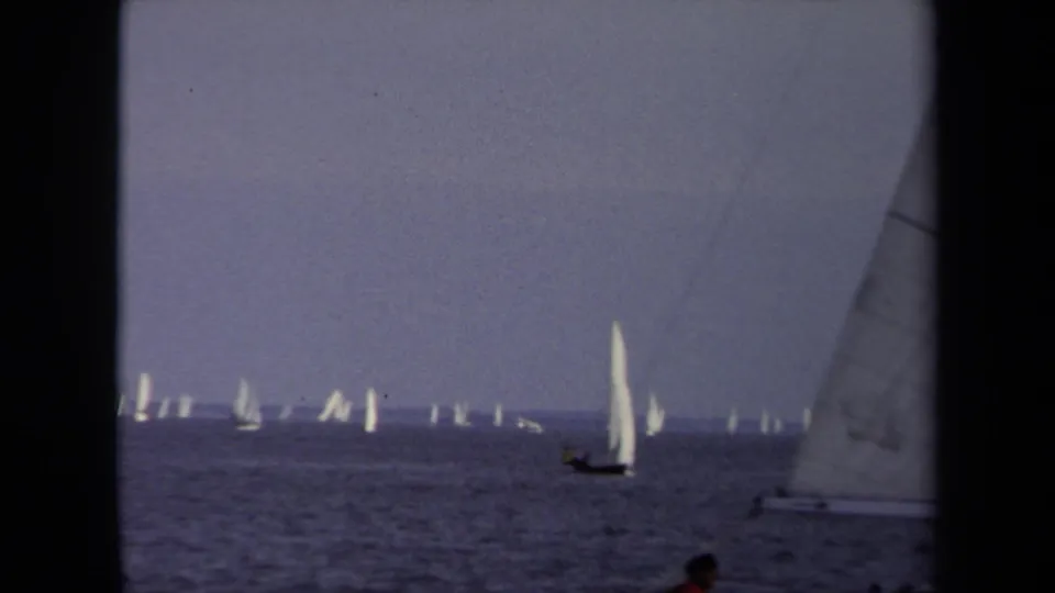 In this 1970 Annapolis home-movie frame, a white sailboat stands out beyond the filming boat's sails.