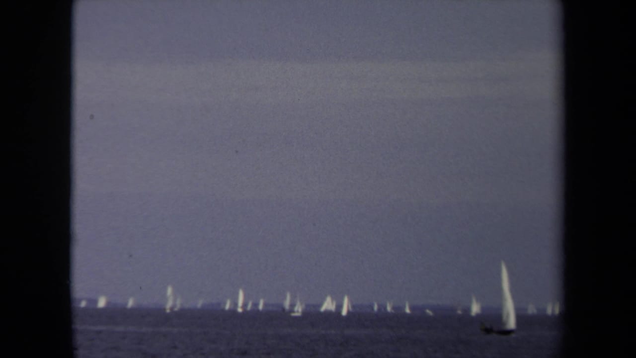 1970 Annapolis sailing view with a line of distant white sails and a single larger sailboat moving near the right side of frame.
