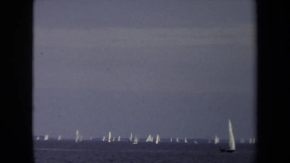 1970 Annapolis sailing view with a line of distant white sails and a single larger sailboat moving near the right side of frame.