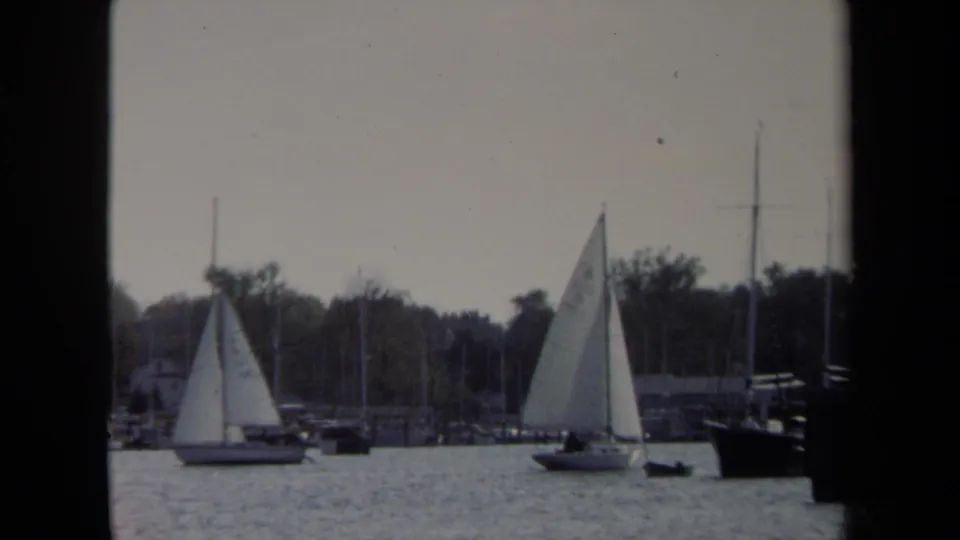1970 8mm Annapolis waterfront frame with sailboats on rippled water, marina masts, shoreline trees, and dark window-like borders.