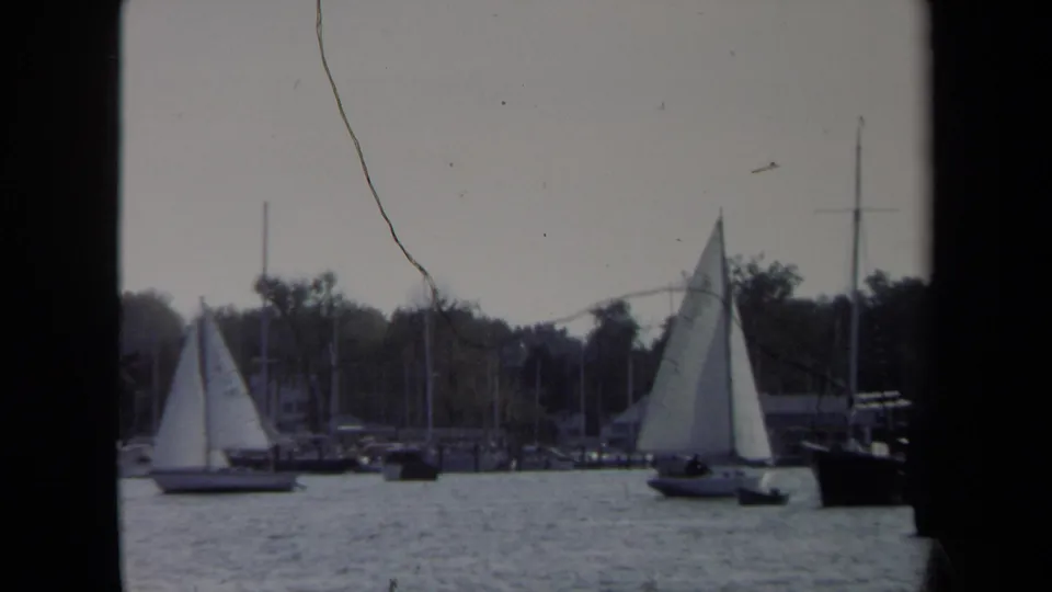 A vintage 8mm view of Annapolis sailboats on calm water, with docked masts and a dark foreground border at the sides.