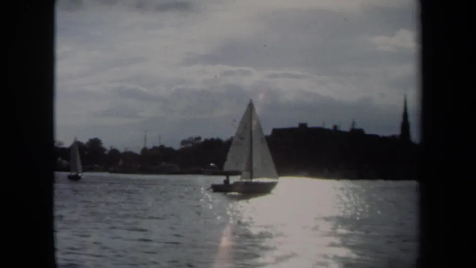 The 1970 Annapolis 8mm frame shows a sailboat against shimmering water, distant buildings, trees, and a steeple-like form on shore.
