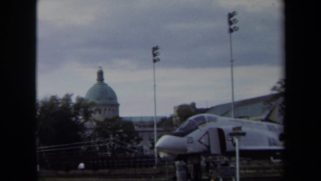 1970 Annapolis 8mm frame showing a military jet display with a domed civic-looking building in the background.