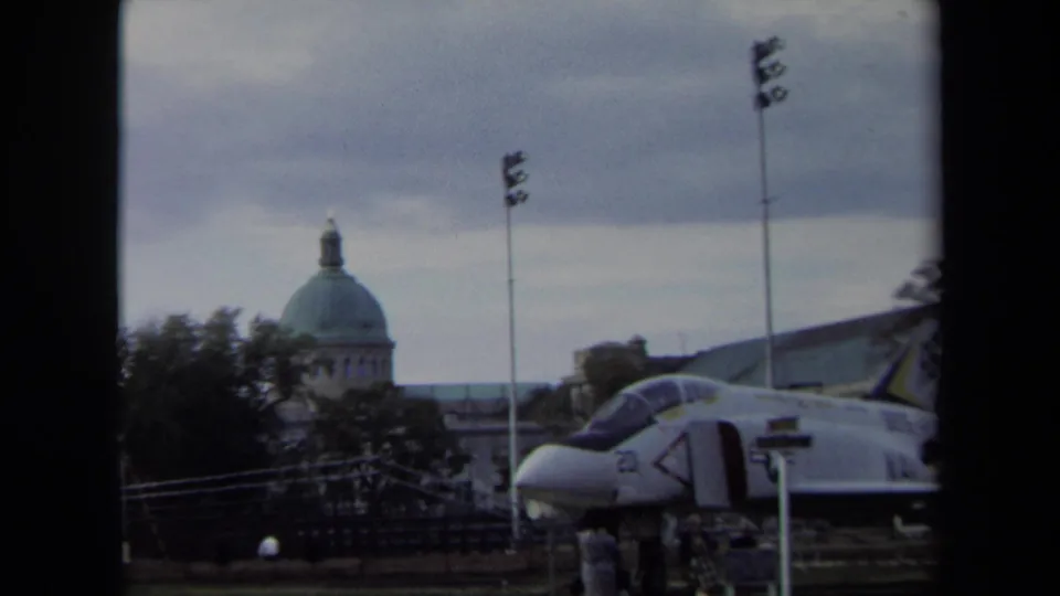 1970 Annapolis 8mm frame showing a military jet display with a domed civic-looking building in the background.