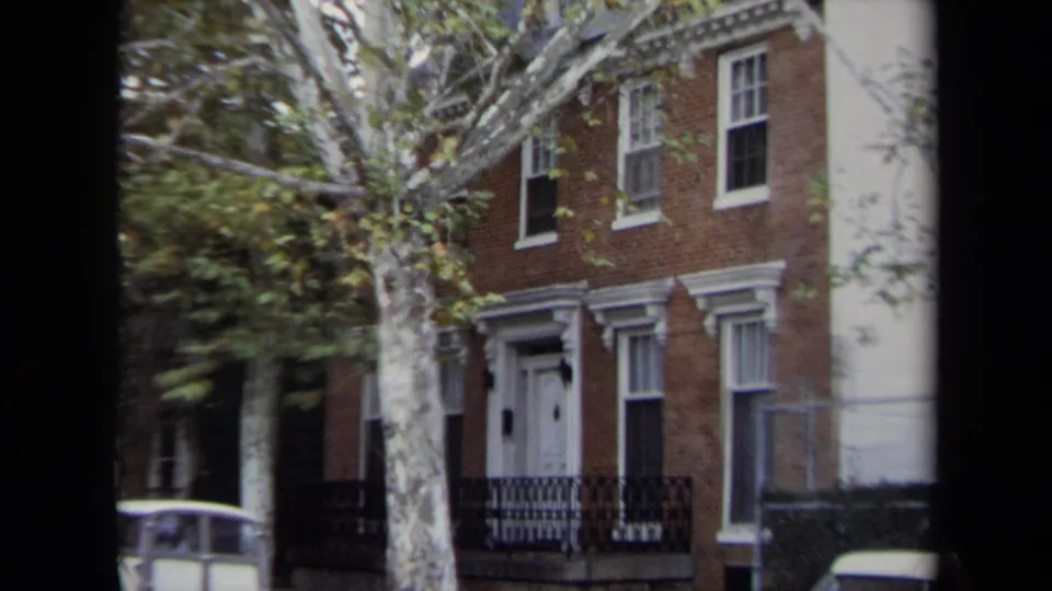 1970 Annapolis 8mm frame showing a brick residential entrance with white trim, iron railing, tree branches, and a parked car.