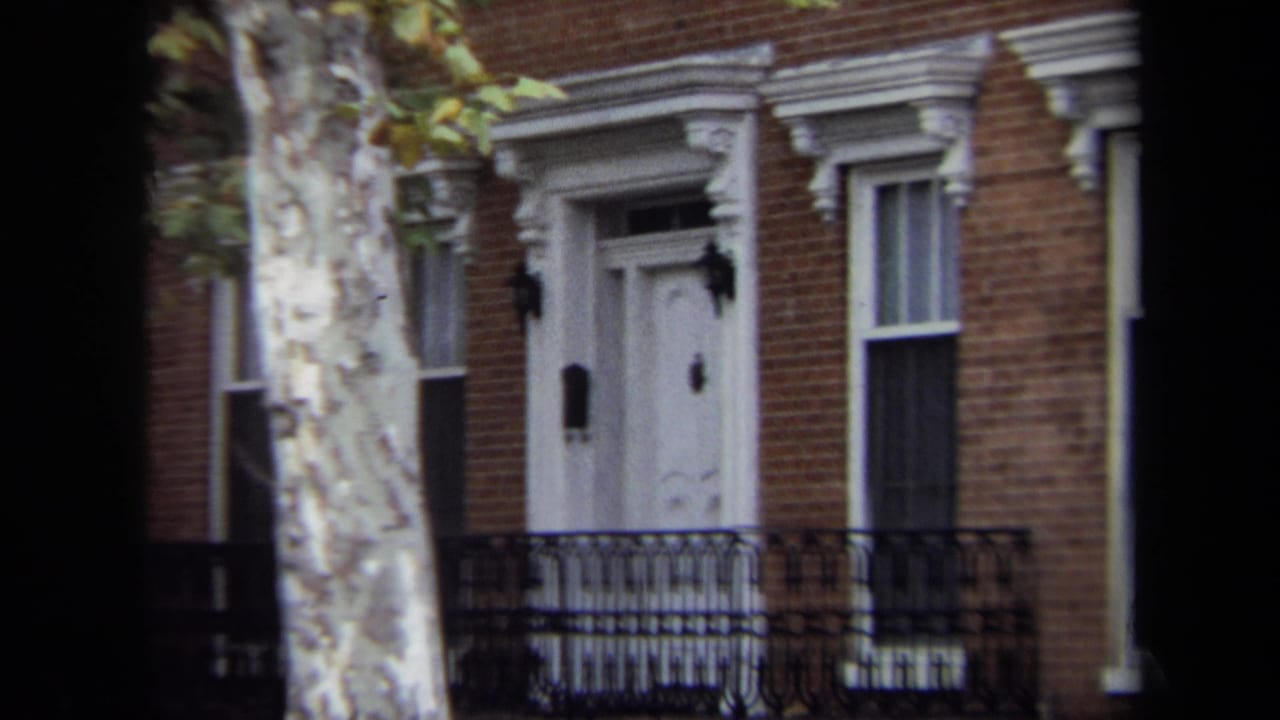 Closer view of a white townhouse door, brick wall, iron fence, and tree trunk.