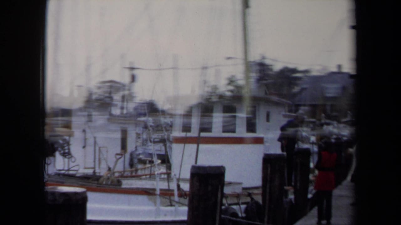 1970 Annapolis harbor view with white boats, mast rigging, dock posts, and a few people standing near the pier.