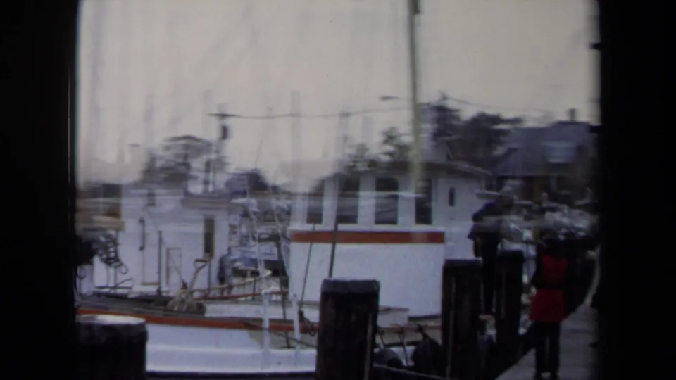 1970 Annapolis harbor view with white boats, mast rigging, dock posts, and a few people standing near the pier.