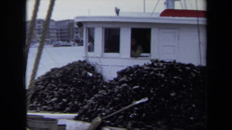 A crew member appears at the cabin window of the docked vessel in Annapolis, with shellfish cargo piled in the foreground.