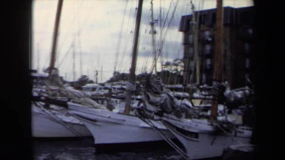 1970 Annapolis 8mm frame showing sailboats moored at a marina, with tall masts and dock structures under cloudy light.