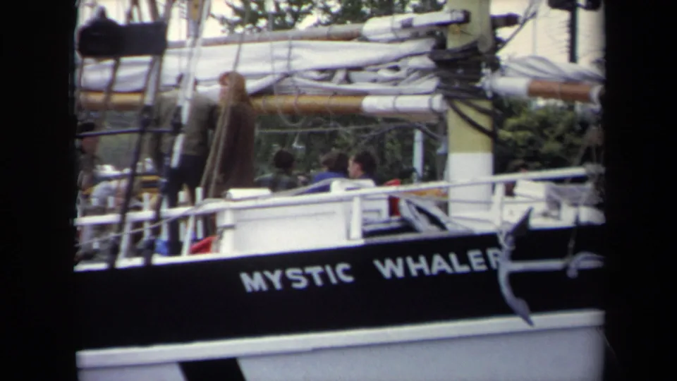 1970 Annapolis marina footage shows the Mystic Whaler name on the dark hull, with people partly visible on deck behind railings and rigging.
