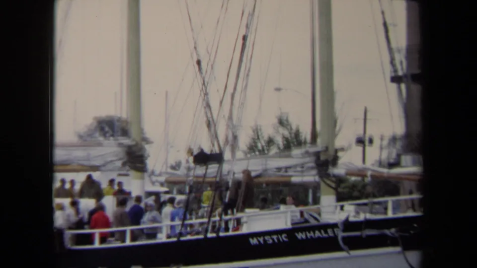 1970 Annapolis marina scene shows the Mystic Whaler docked with a group of people aboard, masts, rigging, and waterfront details in the background.