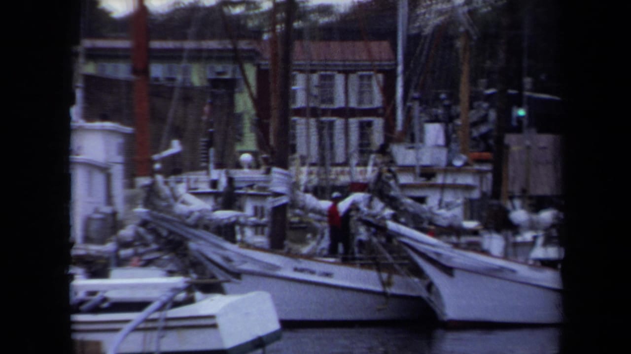 Sailboats moored near brick buildings with people visible on a deck.