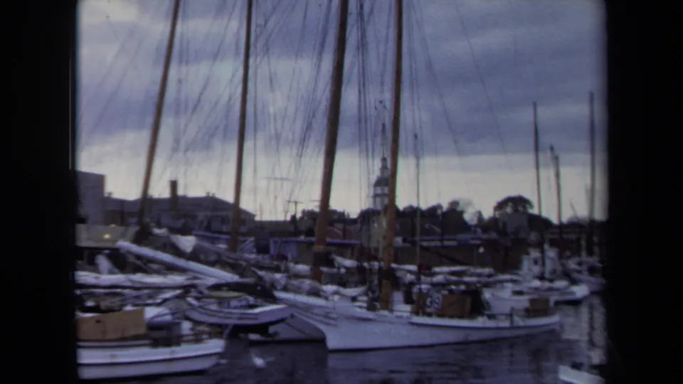 1970 Annapolis harbor scene with sailboats packed along the dock, rigging lines crossing the frame, and town buildings beyond.