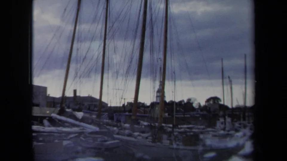 1970 Annapolis harbor view with moored sailboats, vertical masts, dock lines, and soft 8mm color under overcast light.