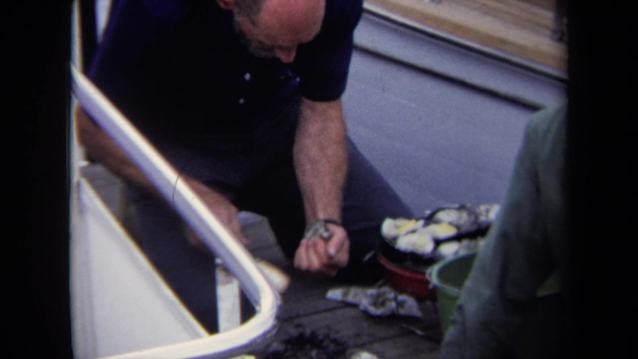 In Annapolis 1970 footage, a man in a blue polo works over oysters on a boat deck as another man in green stands close by.
