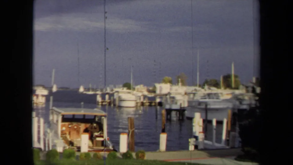 Annapolis harbor opens into a wider view with dock pilings, moored boats, distant shoreline, and a small covered boat in the foreground.