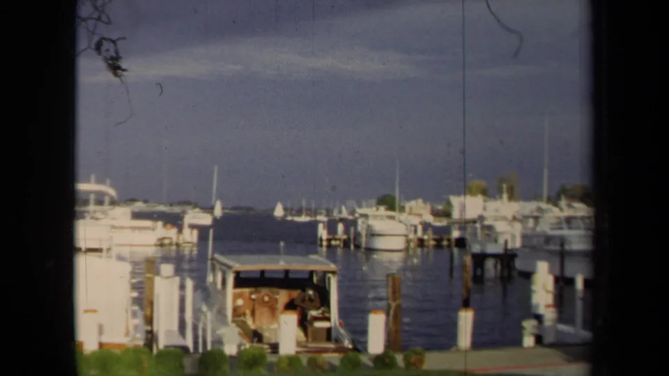 A wider 1970 Annapolis harbor frame shows docked boats, white pilings, open water, distant masts, and shoreline structures.
