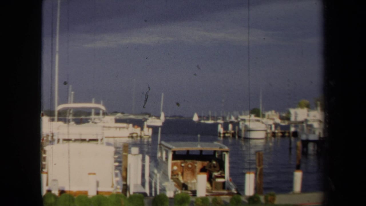 1970 Annapolis marina view with docked motorboats, pilings, open water, and a distant shoreline.