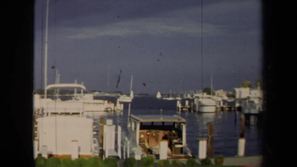 1970 Annapolis marina view with docked motorboats, pilings, open water, and a distant shoreline.
