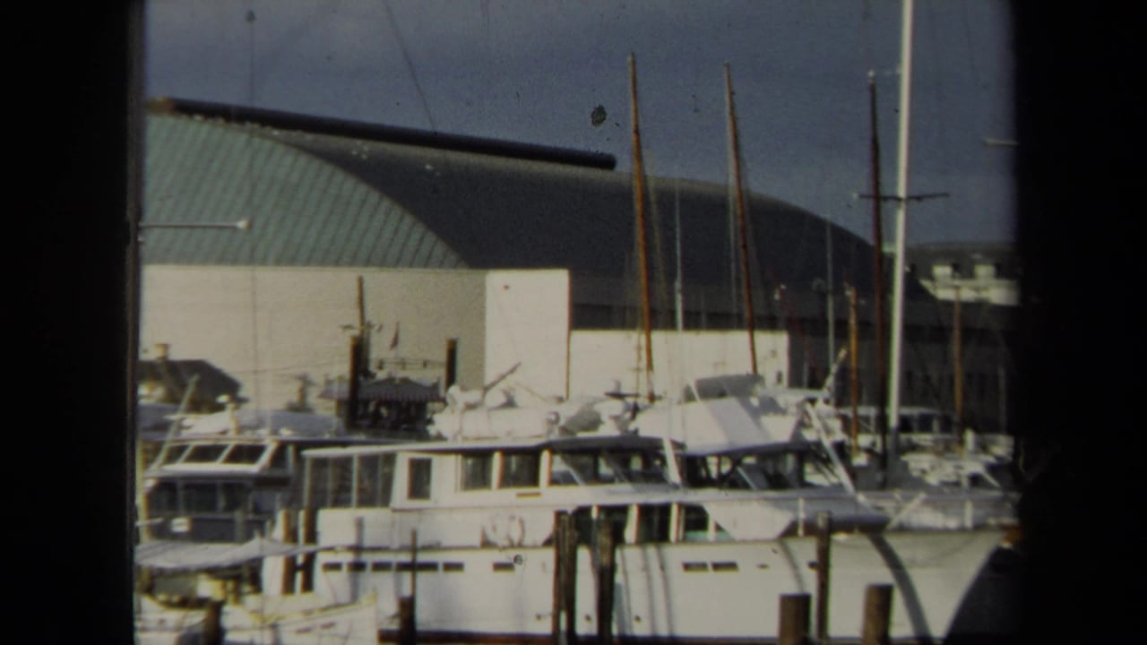 1970 Annapolis close view of yacht cabins and sailboat masts at wooden piers, with the curved green-roof building in the background.