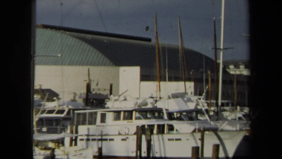 1970 Annapolis close view of yacht cabins and sailboat masts at wooden piers, with the curved green-roof building in the background.