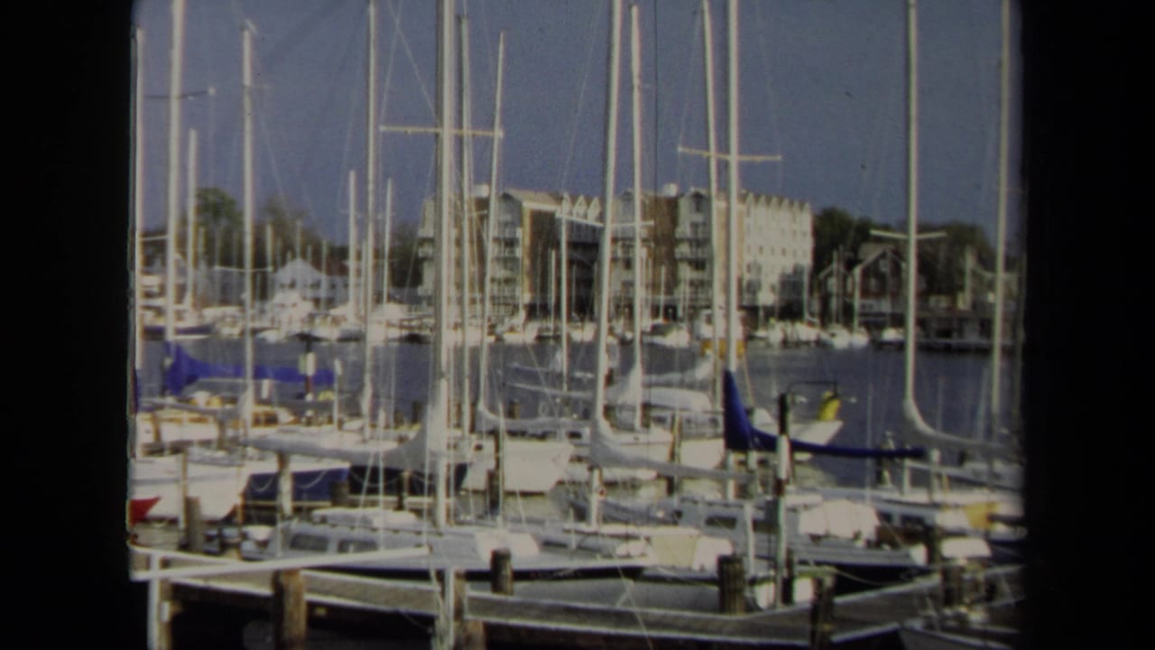Wide 1970 Annapolis marina frame showing dense sailboat masts, moored boats, calm water, dock pilings, and waterfront apartment-like buildings.