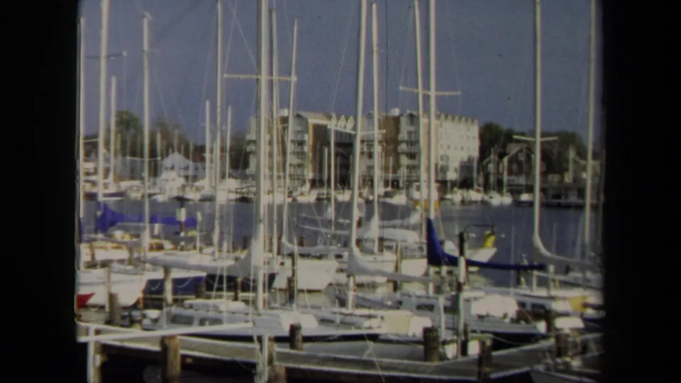Wide 1970 Annapolis marina frame showing dense sailboat masts, moored boats, calm water, dock pilings, and waterfront apartment-like buildings.