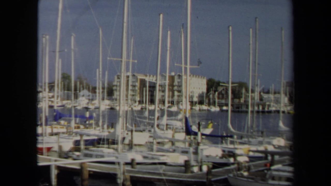 1970 Annapolis marina view with docked sailboats, dense white masts, wooden piers, calm water, and low waterfront buildings in the background.