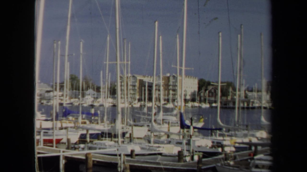 Harbor scene with sailboat masts, docked boats, piers, and waterfront buildings across the water.