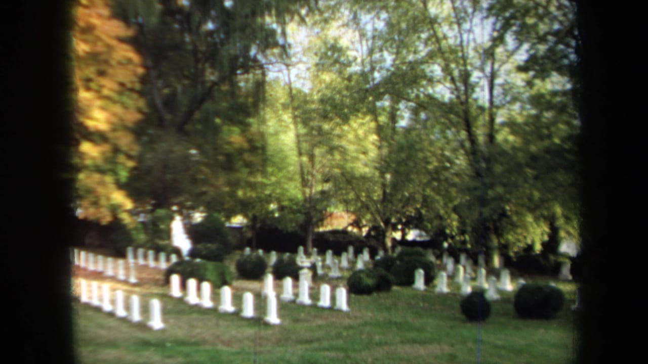 1970 Annapolis 8mm frame showing white military-style headstones, shrubs, and trees in a cemetery landscape.