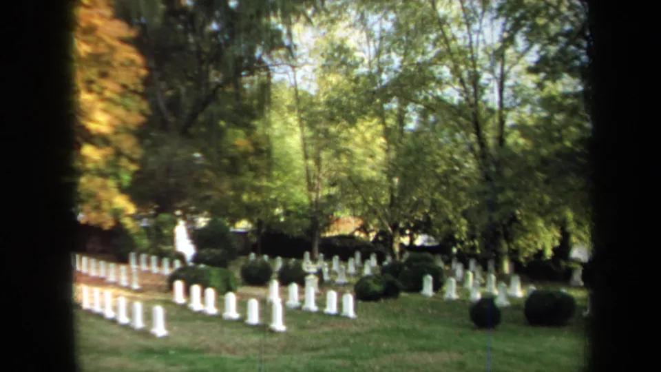 1970 Annapolis 8mm frame showing white military-style headstones, shrubs, and trees in a cemetery landscape.