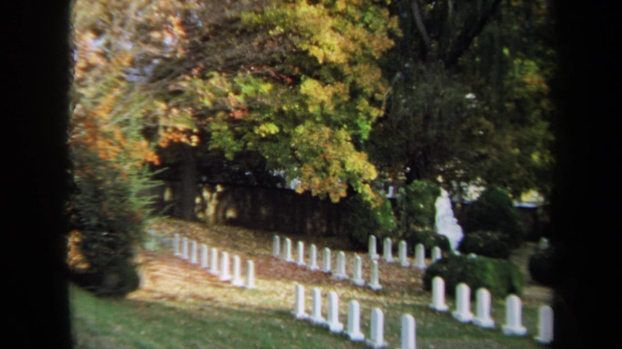 1970 Annapolis home-movie frame showing rows of white headstones among trees with yellow and orange fall leaves.