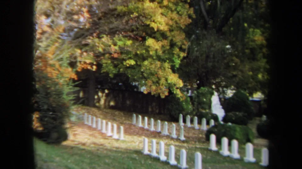 1970 Annapolis home-movie frame showing rows of white headstones among trees with yellow and orange fall leaves.