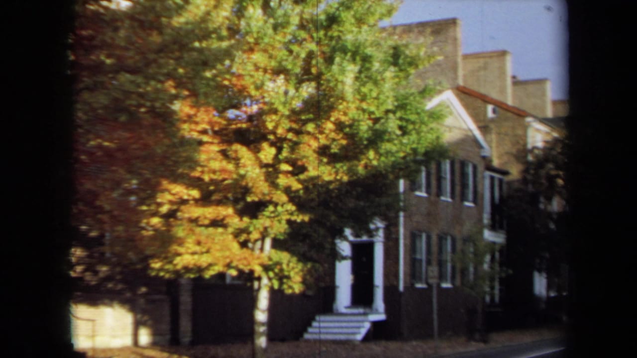 1970 Annapolis home-movie frame showing a golden-leaved tree in front of brick residential buildings and white steps.