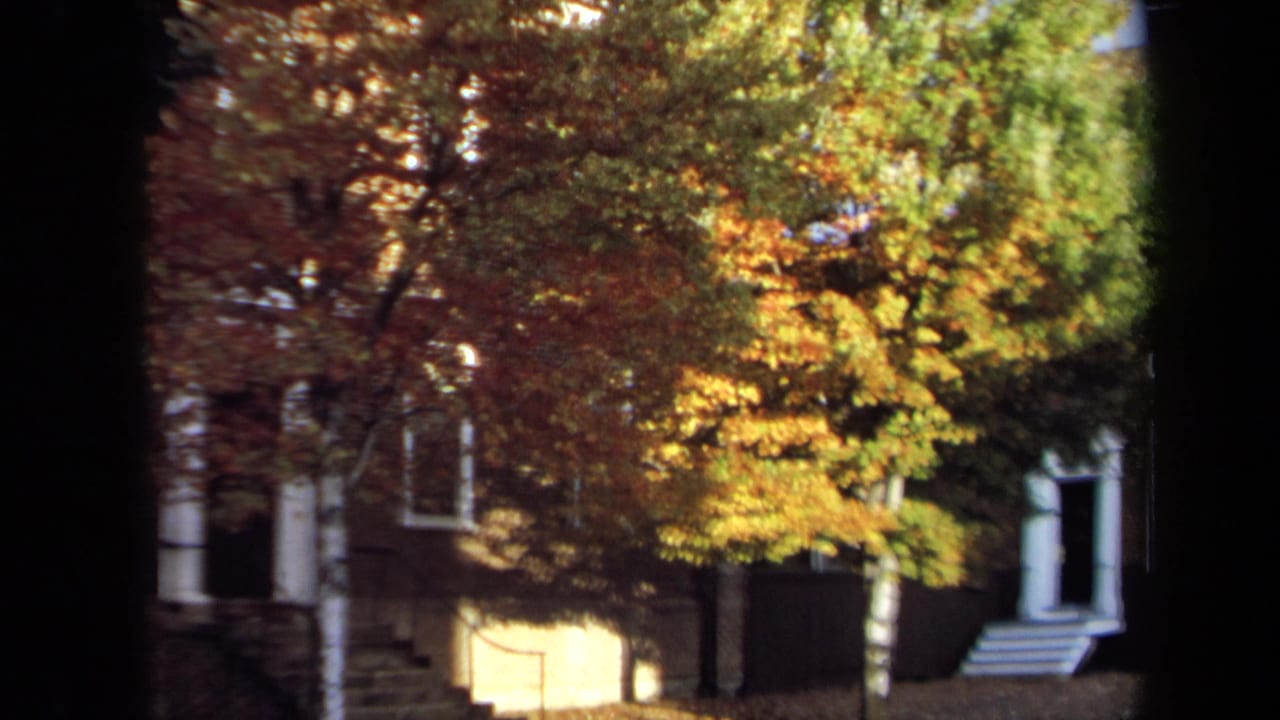 1970 Annapolis home-movie frame showing a brick house facade, exterior steps, and a large tree in autumn color.