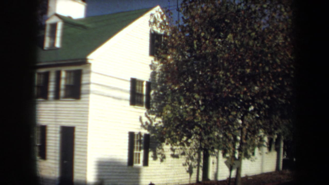 1970 Annapolis frame showing a pale clapboard house with dark shutters and trees along the side of the building.
