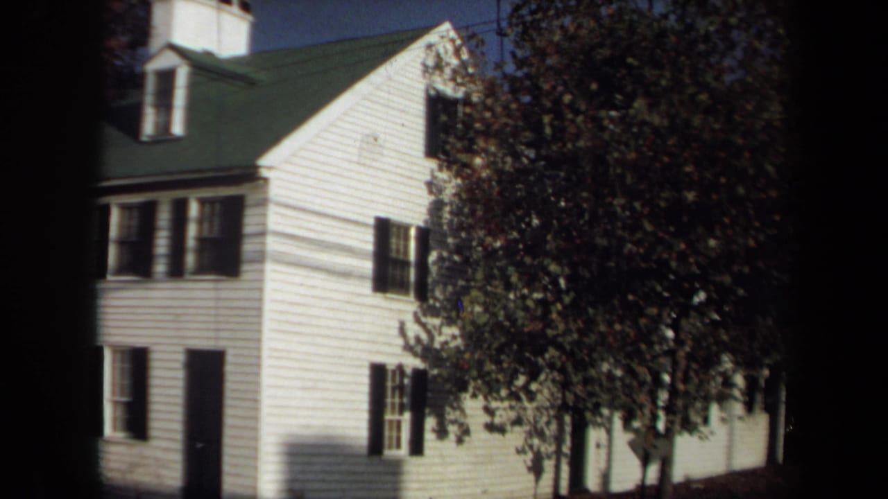1970 Annapolis 8mm frame showing a white clapboard house with black shutters, green roof, dormer, and trees casting shade.