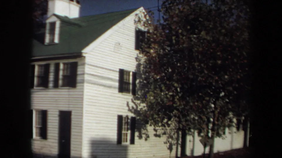 1970 Annapolis 8mm frame showing a white clapboard house with black shutters, green roof, dormer, and trees casting shade.