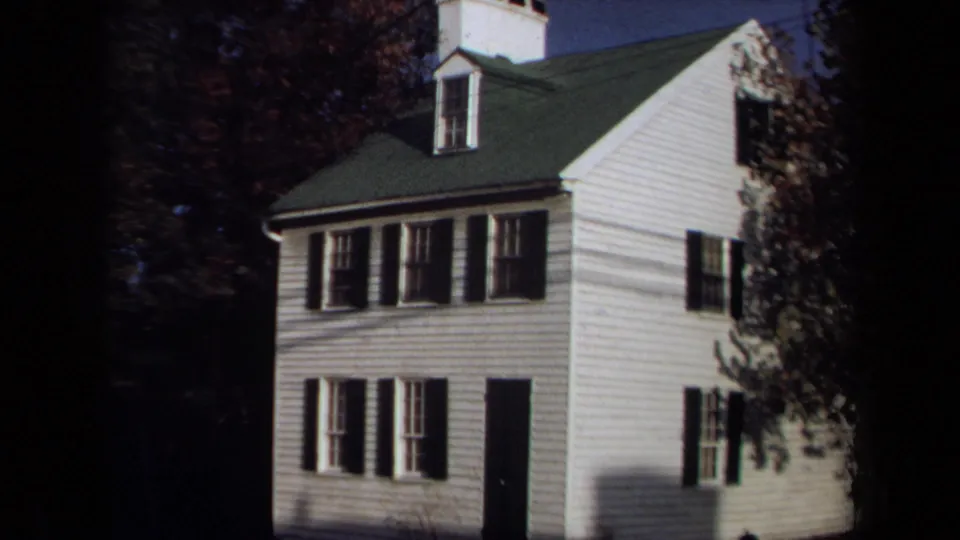 Final 1970 Annapolis frame holds on the white house exterior with black shutters, a green roof, dark doorway, and autumn trees.