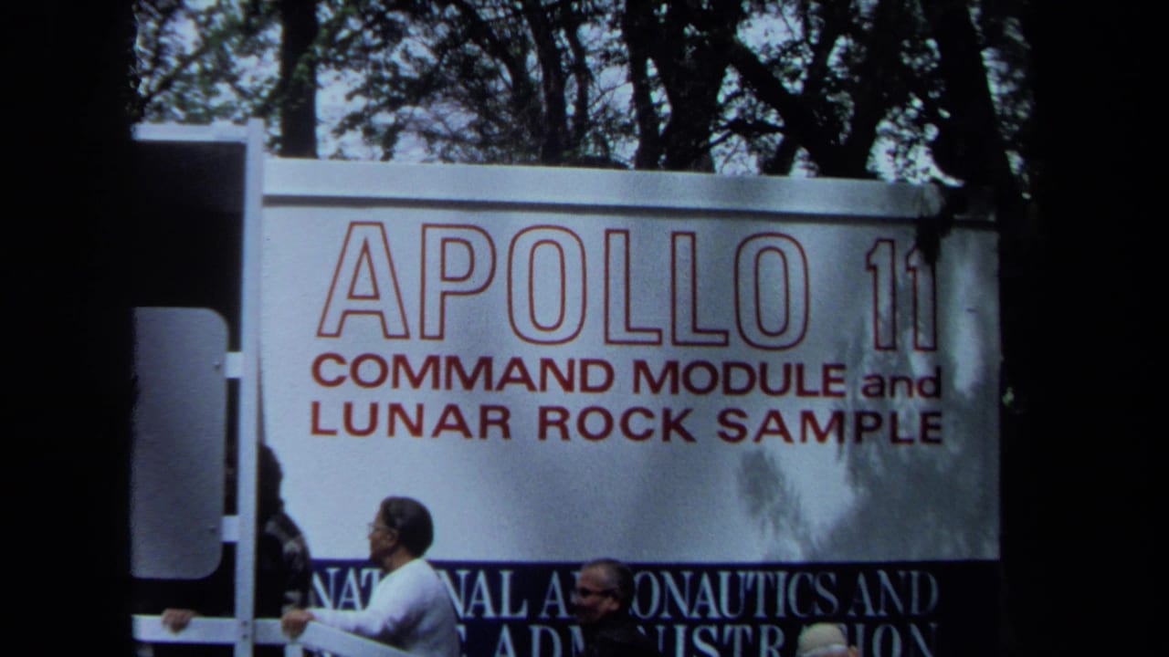 1970 California 8mm frame showing visitors beside a large Apollo 11 command module and lunar rock sample exhibition sign.