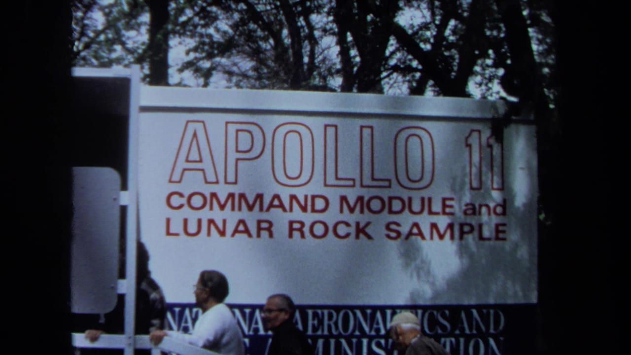 A large Apollo 11 exhibit sign fills the frame as visitors walk below it.