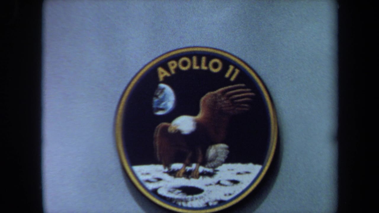 1970s California 8mm frame showing an Apollo 11 mission patch with eagle, moon surface, and Earth artwork.