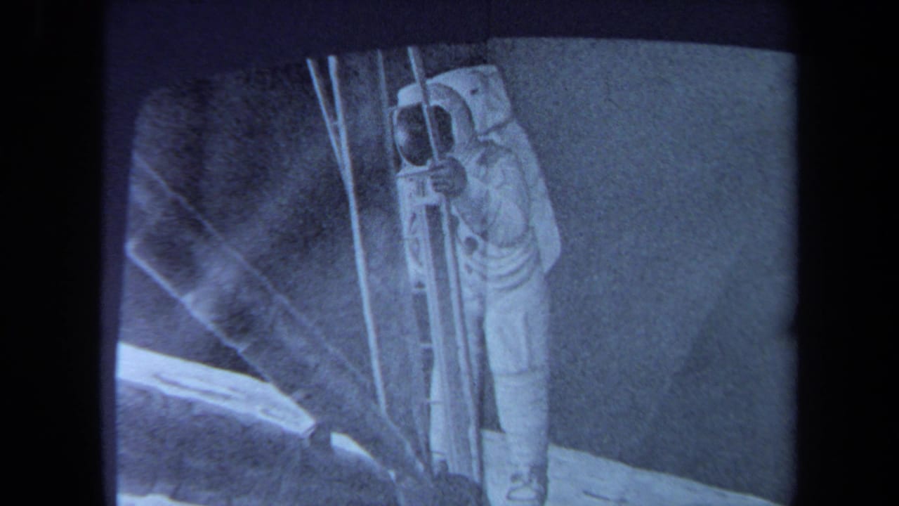 Tight 1970 California home-movie frame of a television screen with an astronaut in a white suit beside ladder-like equipment.