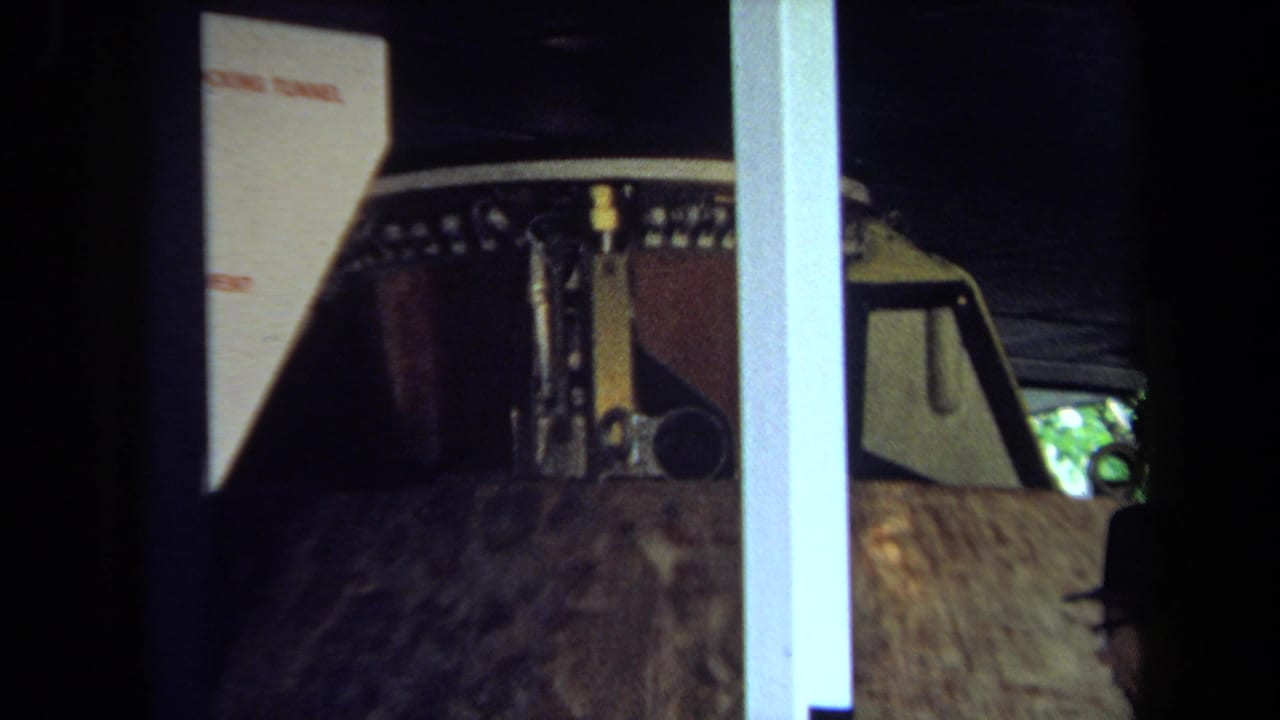 1970 California 8mm frame showing a lunar-module model in a display case, with a partial adult visitor visible at the edge.