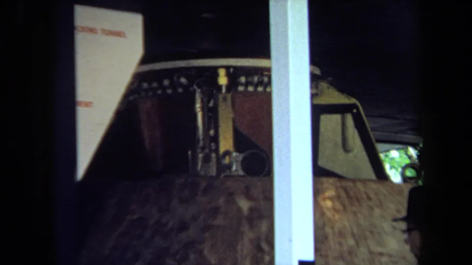 1970 California 8mm frame showing a lunar-module model in a display case, with a partial adult visitor visible at the edge.
