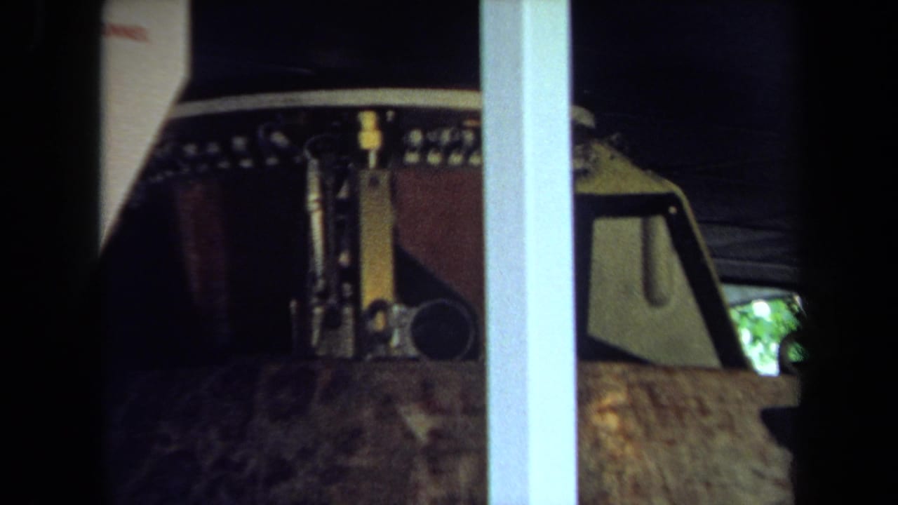1970 California 8mm frame showing part of a brown parade float component behind glass with metal details and interior supports.