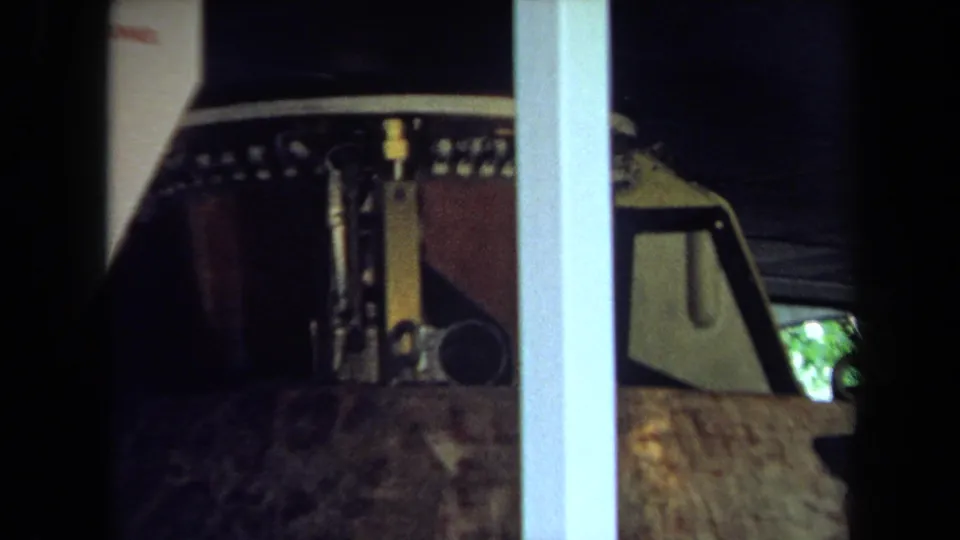 1970 California 8mm frame showing part of a brown parade float component behind glass with metal details and interior supports.